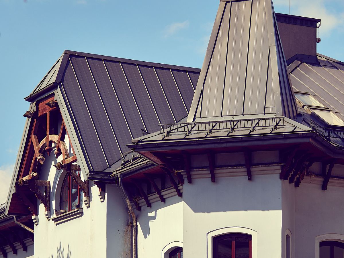 Licensed stock photograph: a dark standing seam metal roof with a steep sheet metal dormer and a run of snow rail above the eave.